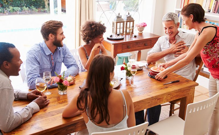 A group of people are gathered around a table, celebrating a birthday with a cake.